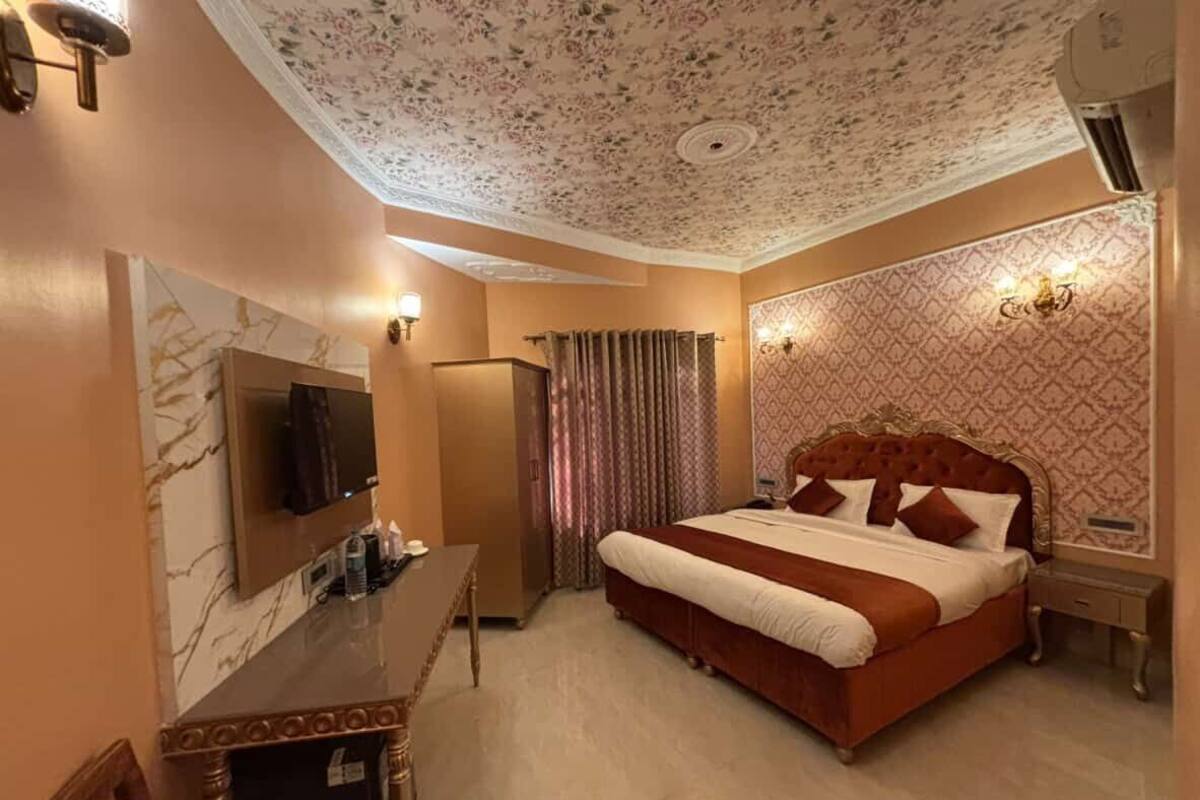 A hotel room with a large bed, a desk, a television, and a ceiling with floral patterns.