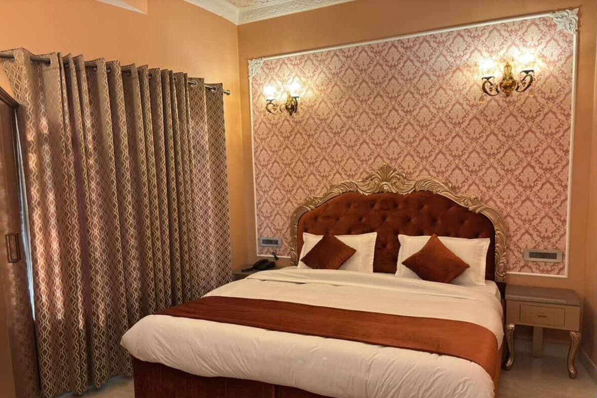 A large bed with a wooden headboard, two wall sconces, and a patterned wallpaper.