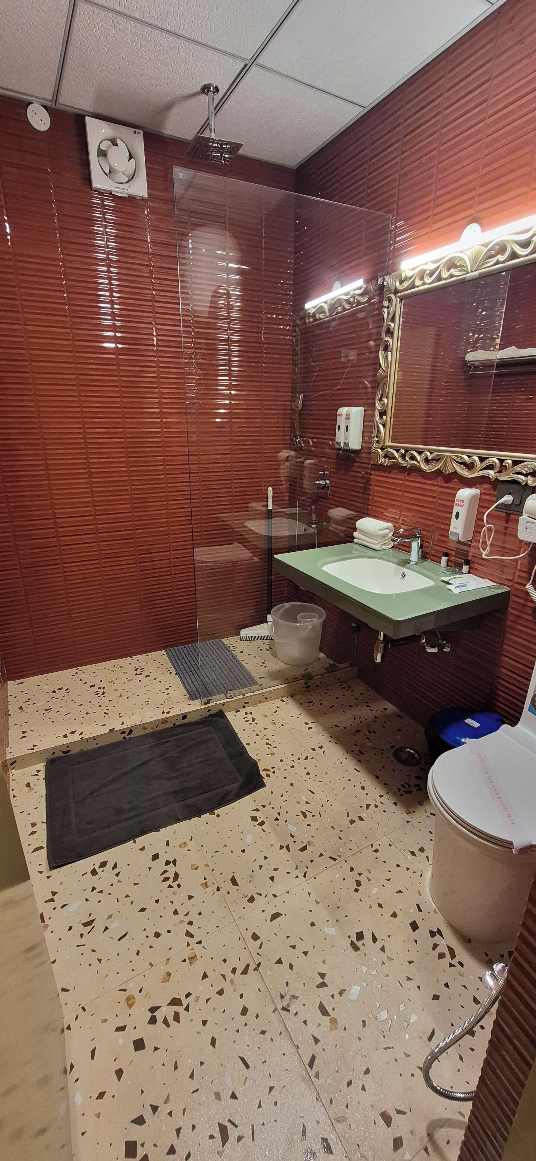A bathroom with a red tiled wall, a green sink, a mirror, and a shower.