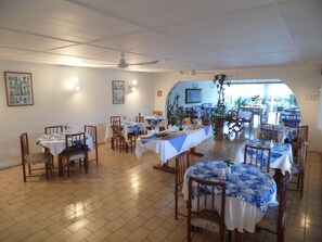 A dining area with multiple tables, chairs, ceiling fans, and potted plants.