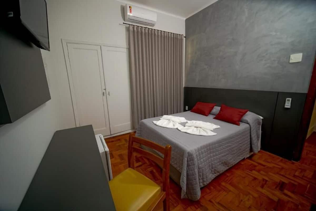Ein Schlafzimmer mit einem Bett, einem Schreibtisch, einem Stuhl, einem Kleiderschrank und einer Klimaanlage.