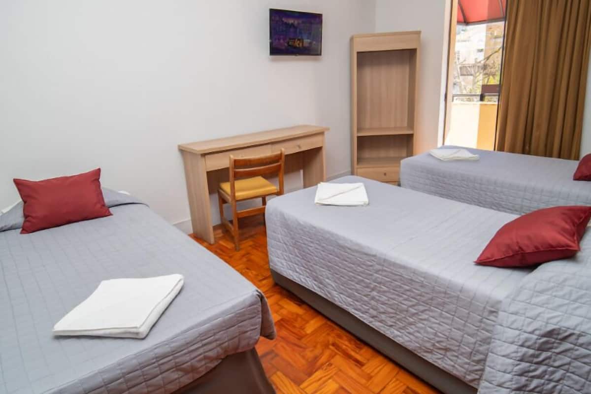 Ein Zimmer mit drei Betten, einem Schreibtisch und einem fensterbepflanzten Fenster.