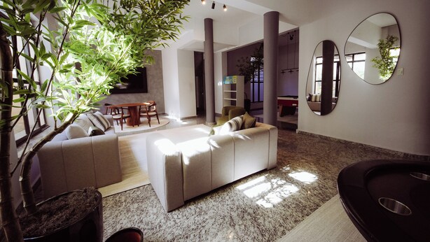 A modern living room with a sofa, a coffee table, and a potted plant. - Hotel Euro Suíte Poços de Caldas By Nacional Inn (Poços de Caldas)
