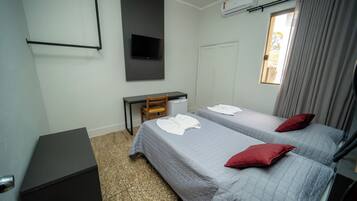 A hotel room with two beds, a desk, a chair, a TV, and an air conditioning unit.