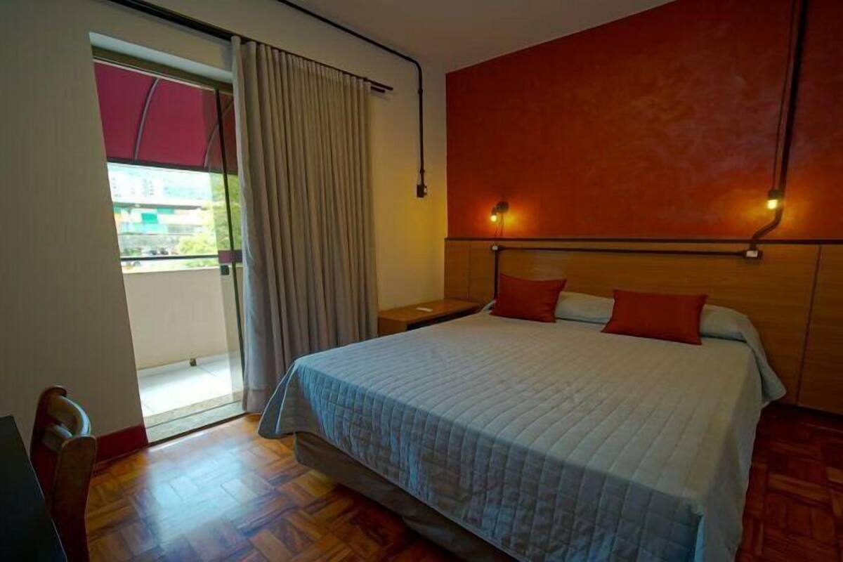 Ein Hotelzimmer mit Bett, Nachttisch, Holzboden und Blick durch eine Glastür.