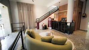 A lobby with a reception desk, a staircase, a green sofa, and a coffee machine. - Hotel Euro Suíte Poços de Caldas By Nacional Inn (Poços de Caldas)