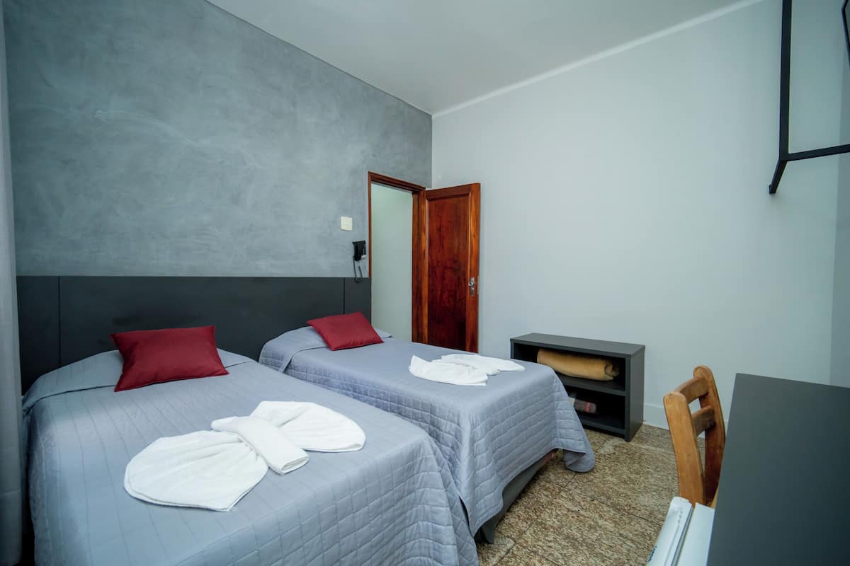 Ein Hotelzimmer mit zwei Betten, einer Holztür, einem kleinen Schreibtisch und einem Stuhl.