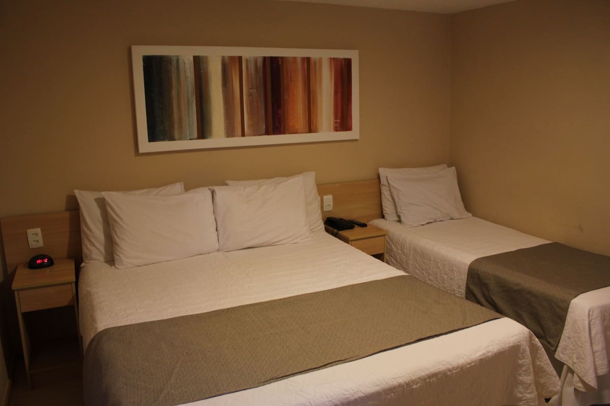 Een hotelkamer met twee eenpersoonsbedden, een nachtkastje met een telefoon en een wekker, en een schilderij aan de muur.
