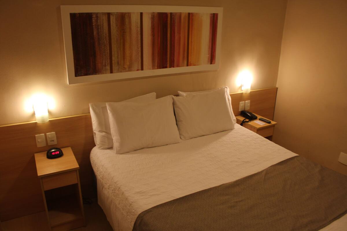 Een hotelkamer met een bed, twee nachtkastjes, een klok en een kunstwerk aan de muur.