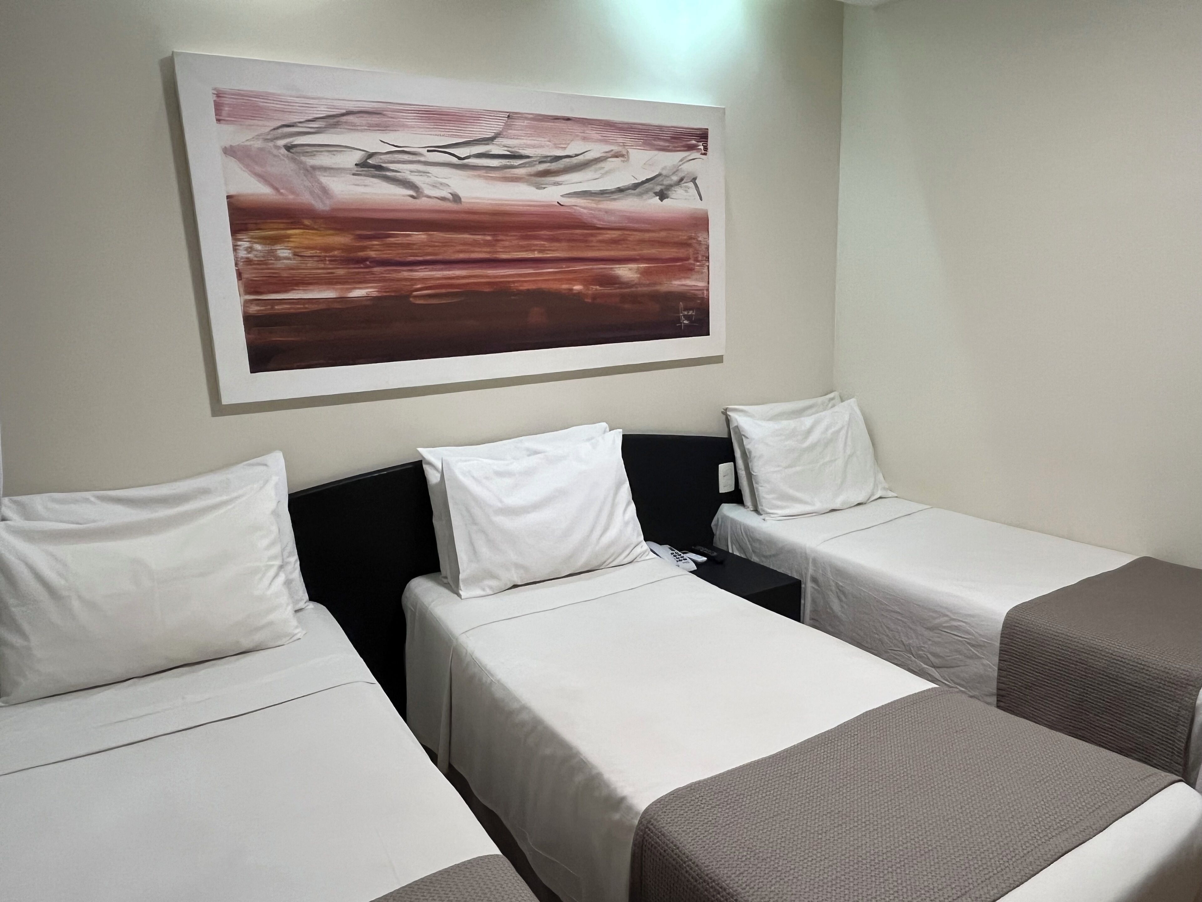 A hotel room with two single beds, each with white linens and a headboard. There is a painting on the wall above the beds.