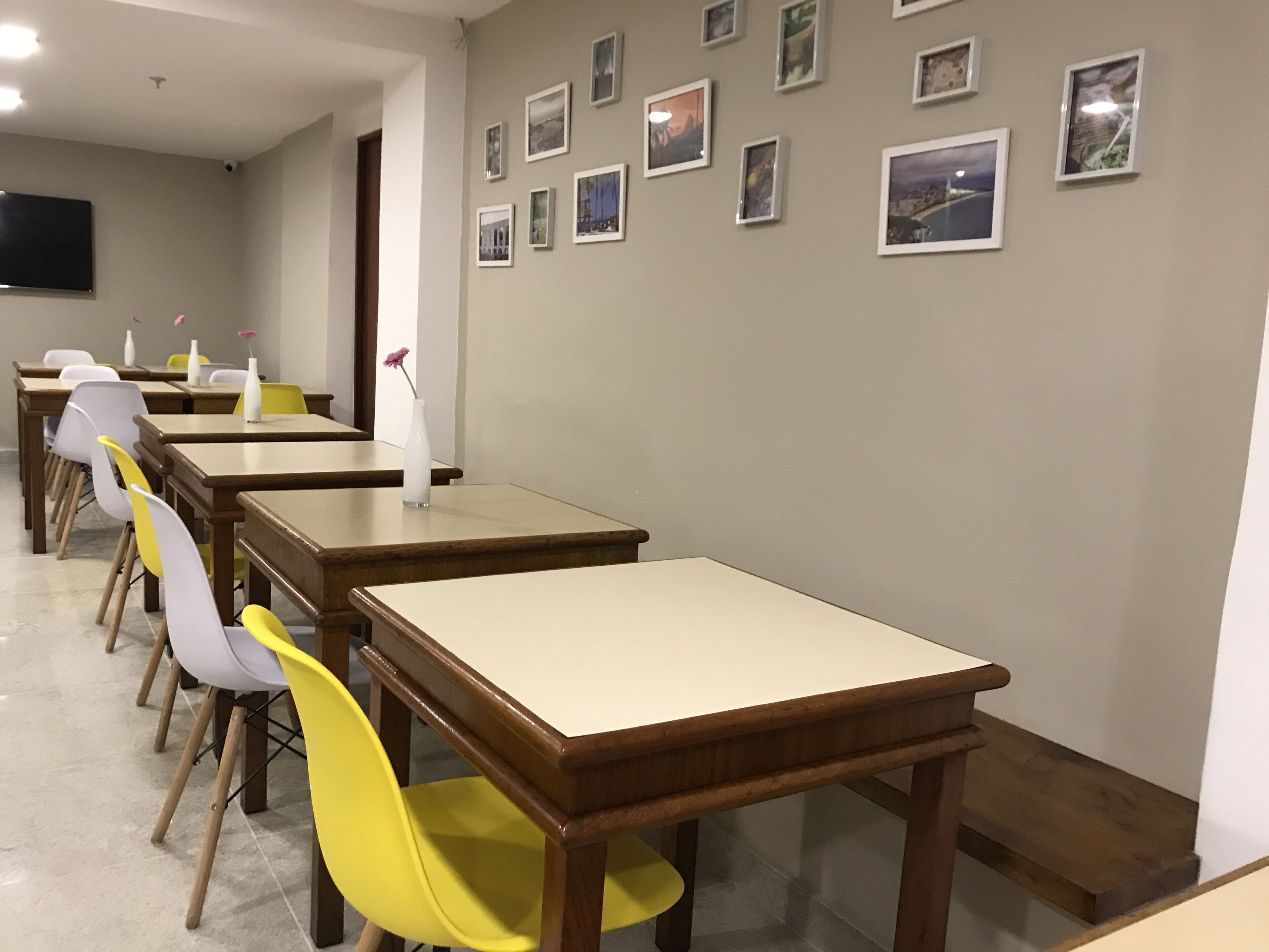 A dining area with multiple tables and chairs, a wall with framed pictures, and a flat-screen TV mounted on the wall.