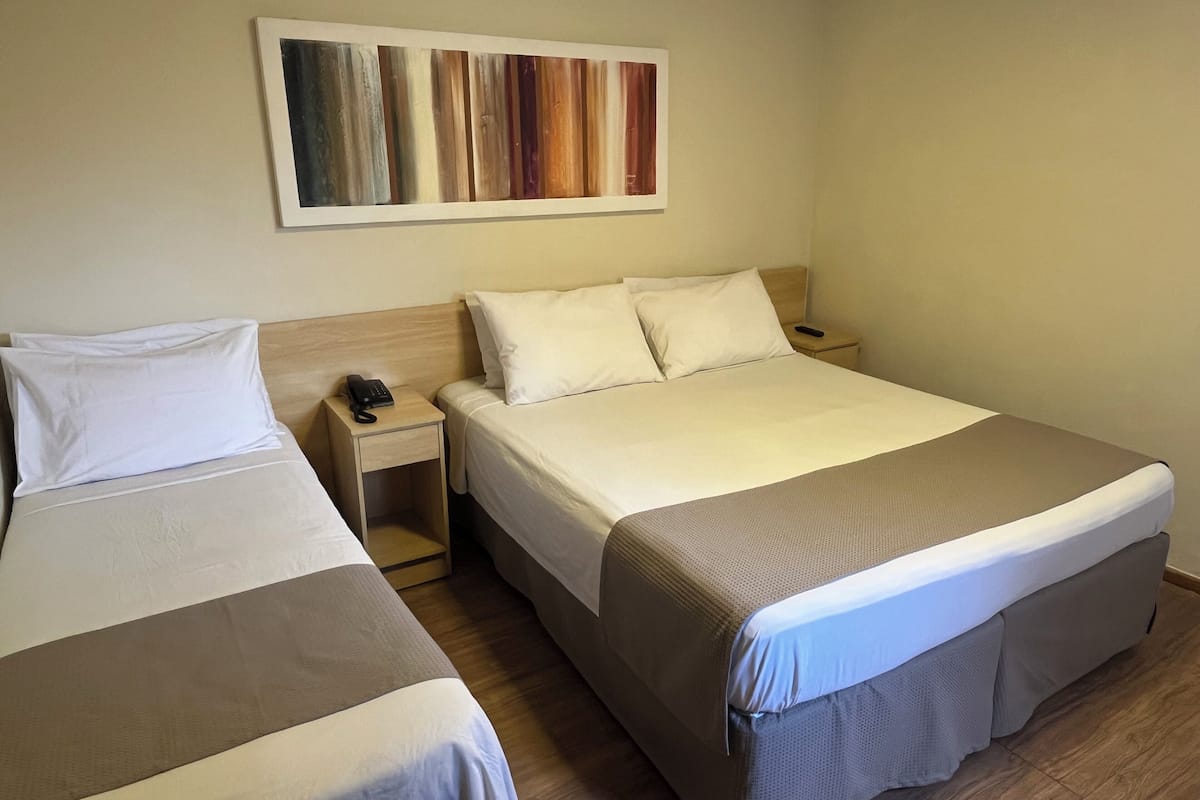 Een hotelkamer met twee bedden, een houten hoofdbord, een nachtkastje met een telefoon en een kunstwerk aan de muur.
