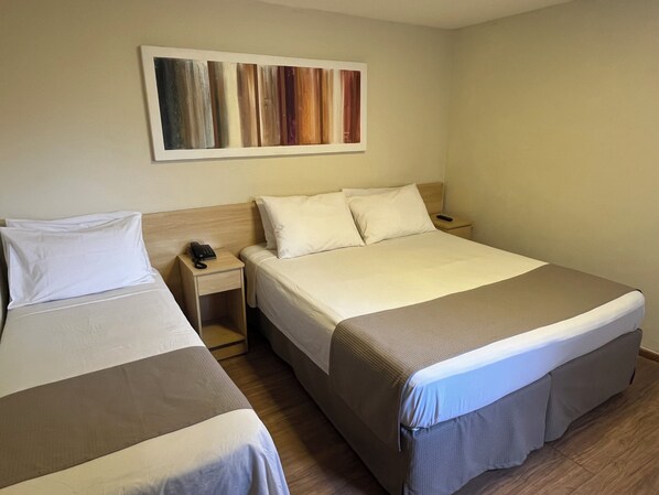 Habitación de hotel con dos camas, un cabecero de madera, una mesita de noche con teléfono y una obra de arte colgada en la pared.