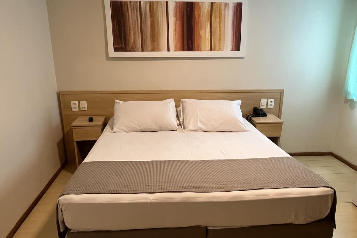 Een hotelkamer met een groot bed, twee nachtkastjes, een wandtelefoon en een schilderij boven het bed.