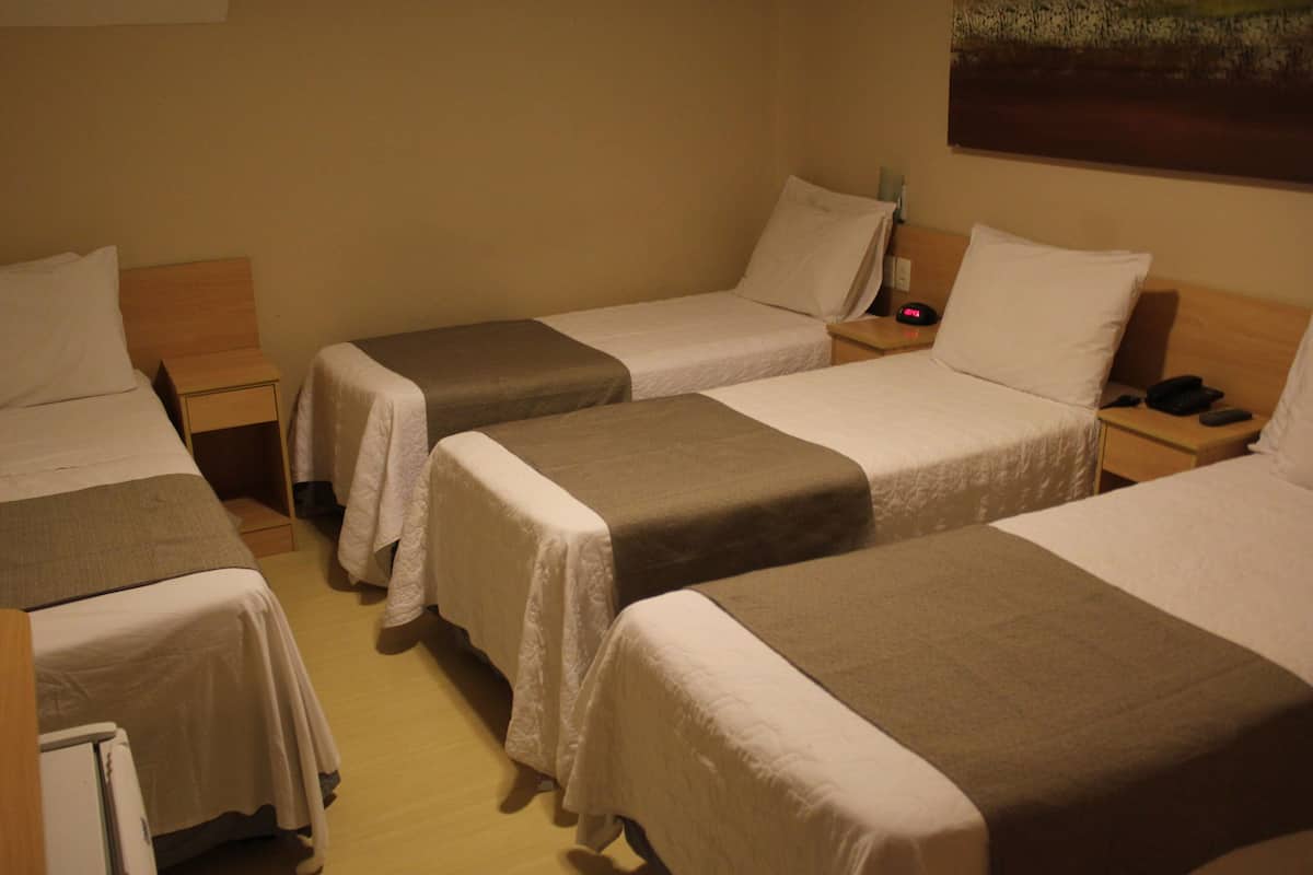 Een hotelkamer met drie eenpersoonsbedden, elk voorzien van een nachtkastje en een lamp.