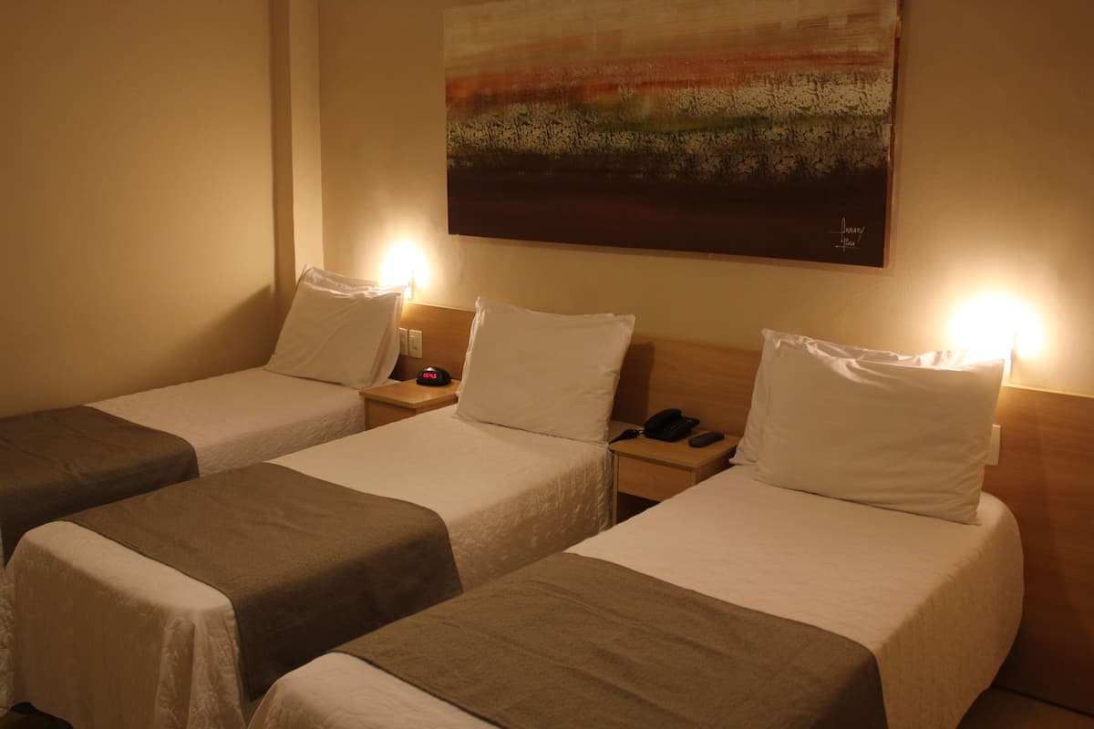 Een hotelkamer met drie eenpersoonsbedden, elk voorzien van nachtkastje, lamp en telefoon.
