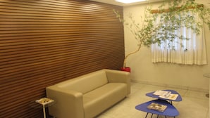 Une pièce moderne avec un mur lambrissé en bois, un canapé beige, une petite table en verre et une chaise bleue avec des magazines.
