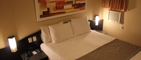 Habitación de hotel con una cama grande, una mesita de noche con teléfono y lámpara, y aire acondicionado de pared.