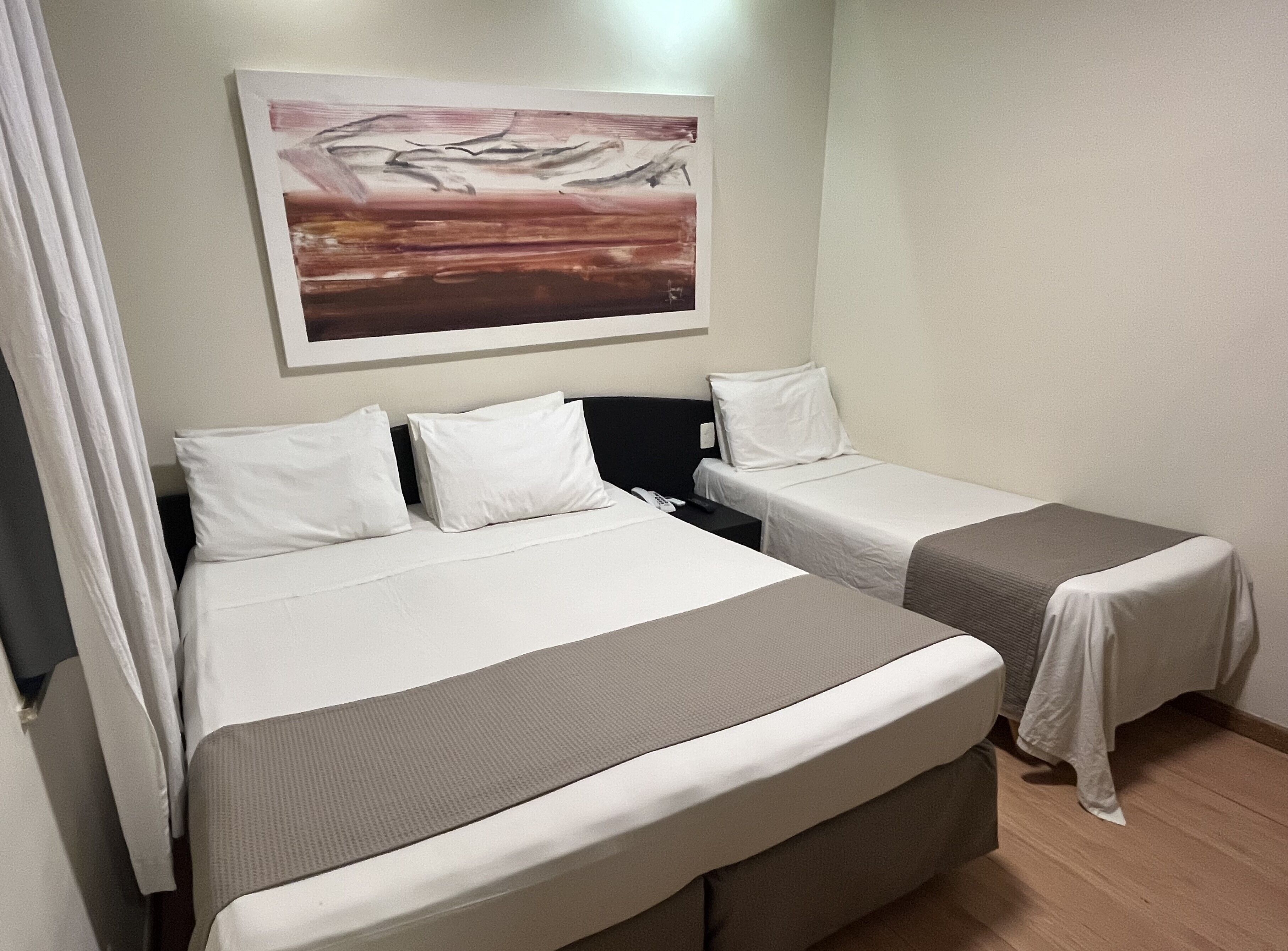 Una habitación de hotel con dos camas, un cuadro en la pared y una cortina.