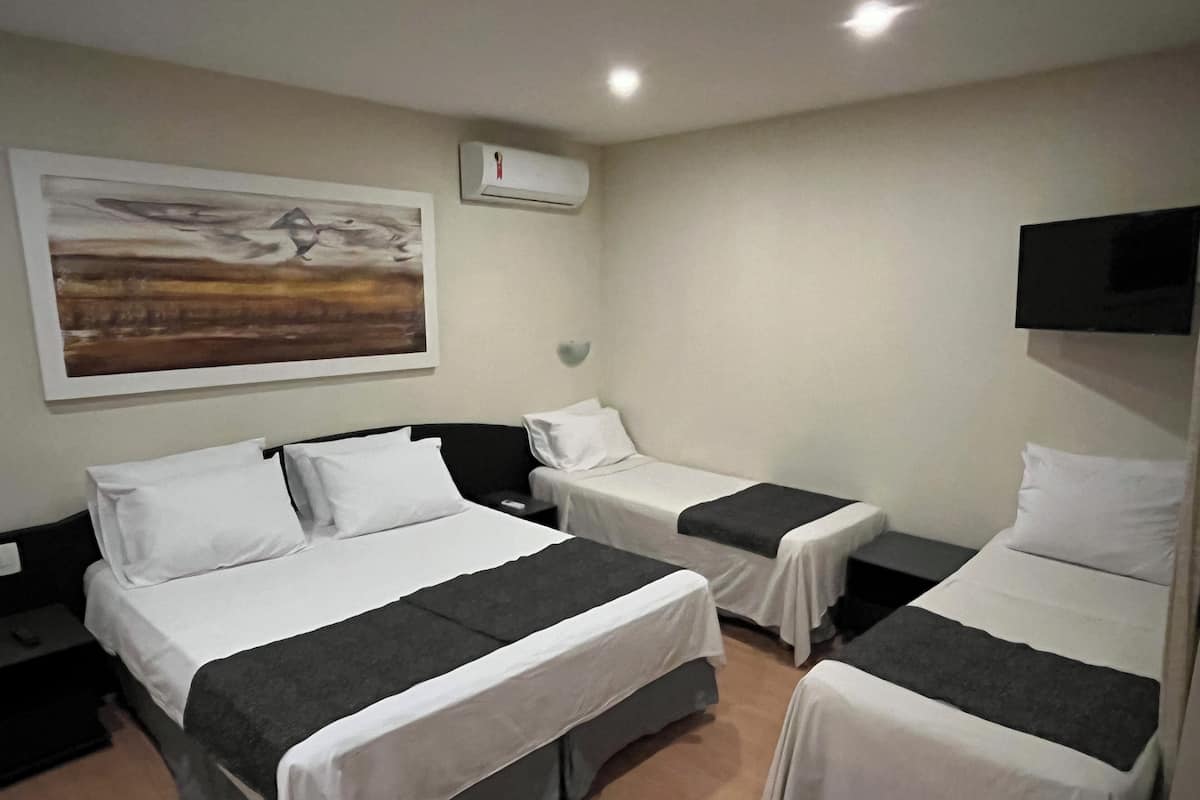 Een hotelkamer met drie eenpersoonsbedden, een schilderij aan de muur, een airconditioning en een aan de wand bevestigde televisie.