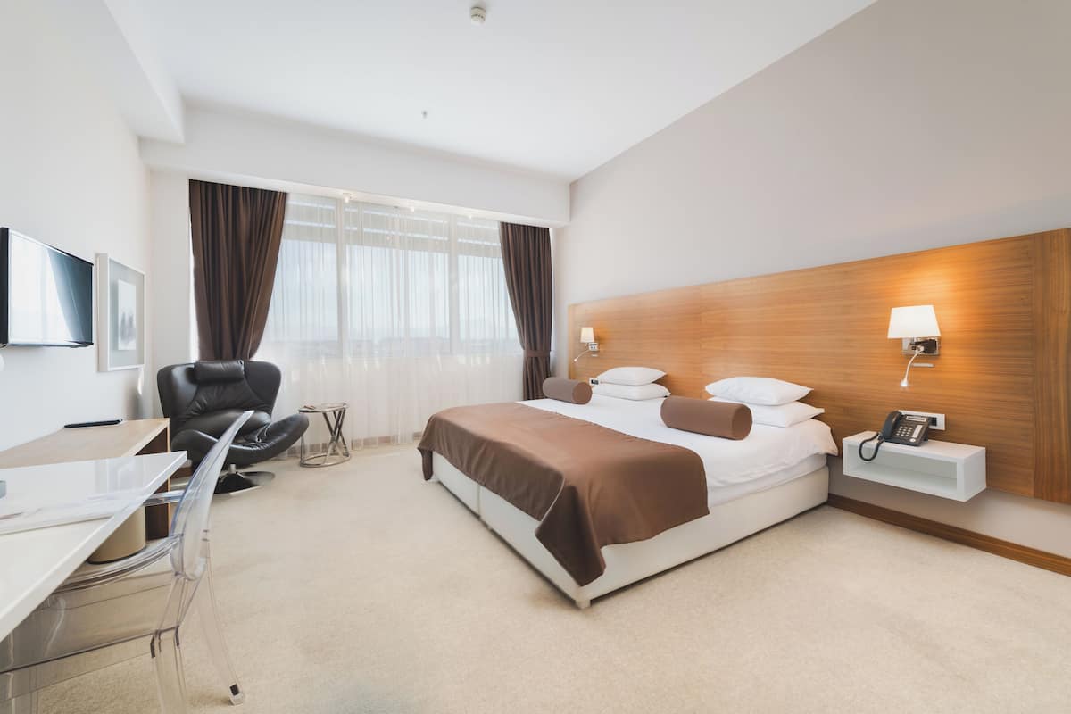 Ein modernes Hotelzimmer mit Bett, Schreibtisch, Stuhl und Nachttisch mit Lampe.