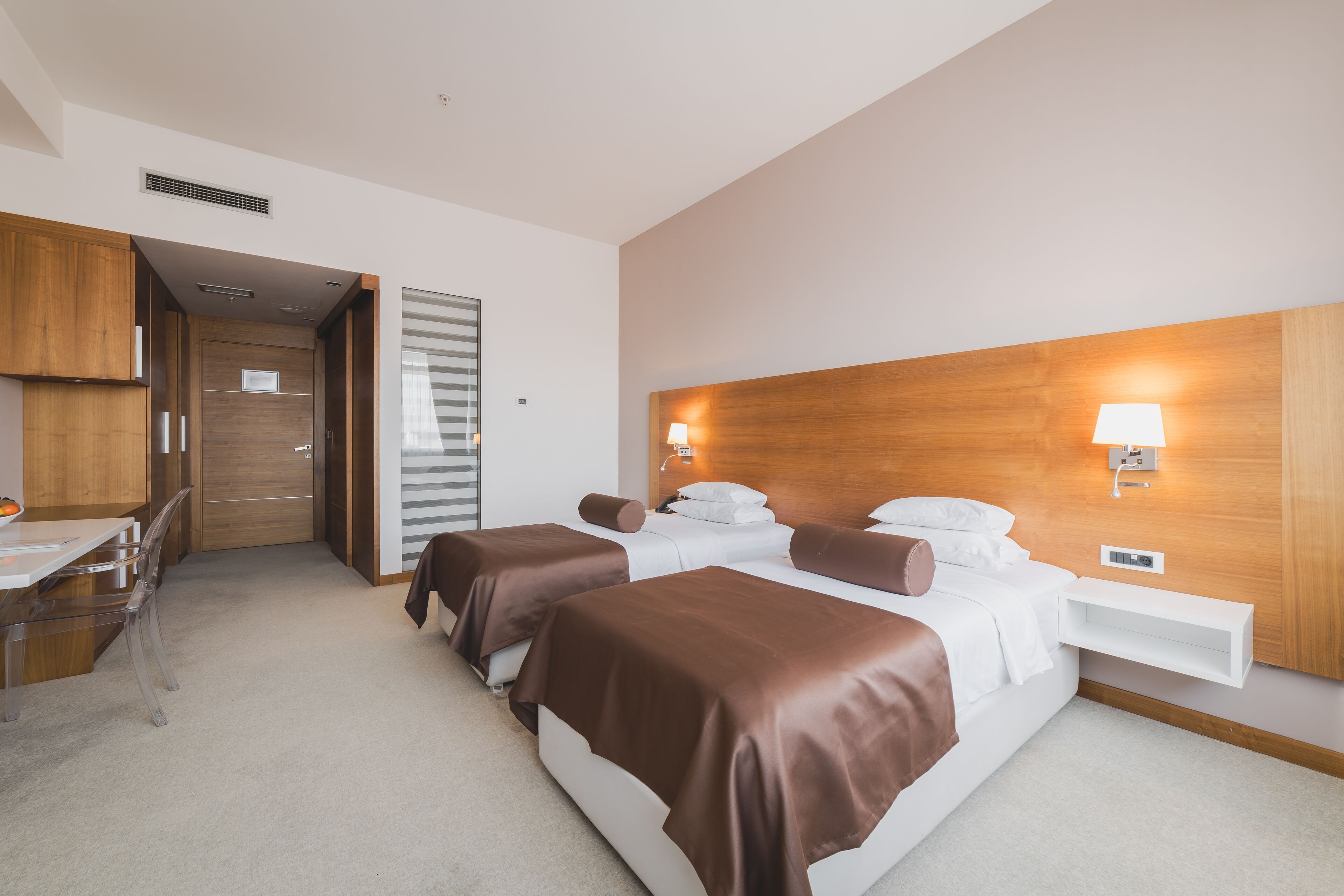 A hotel room with two beds, a desk, and a chair.