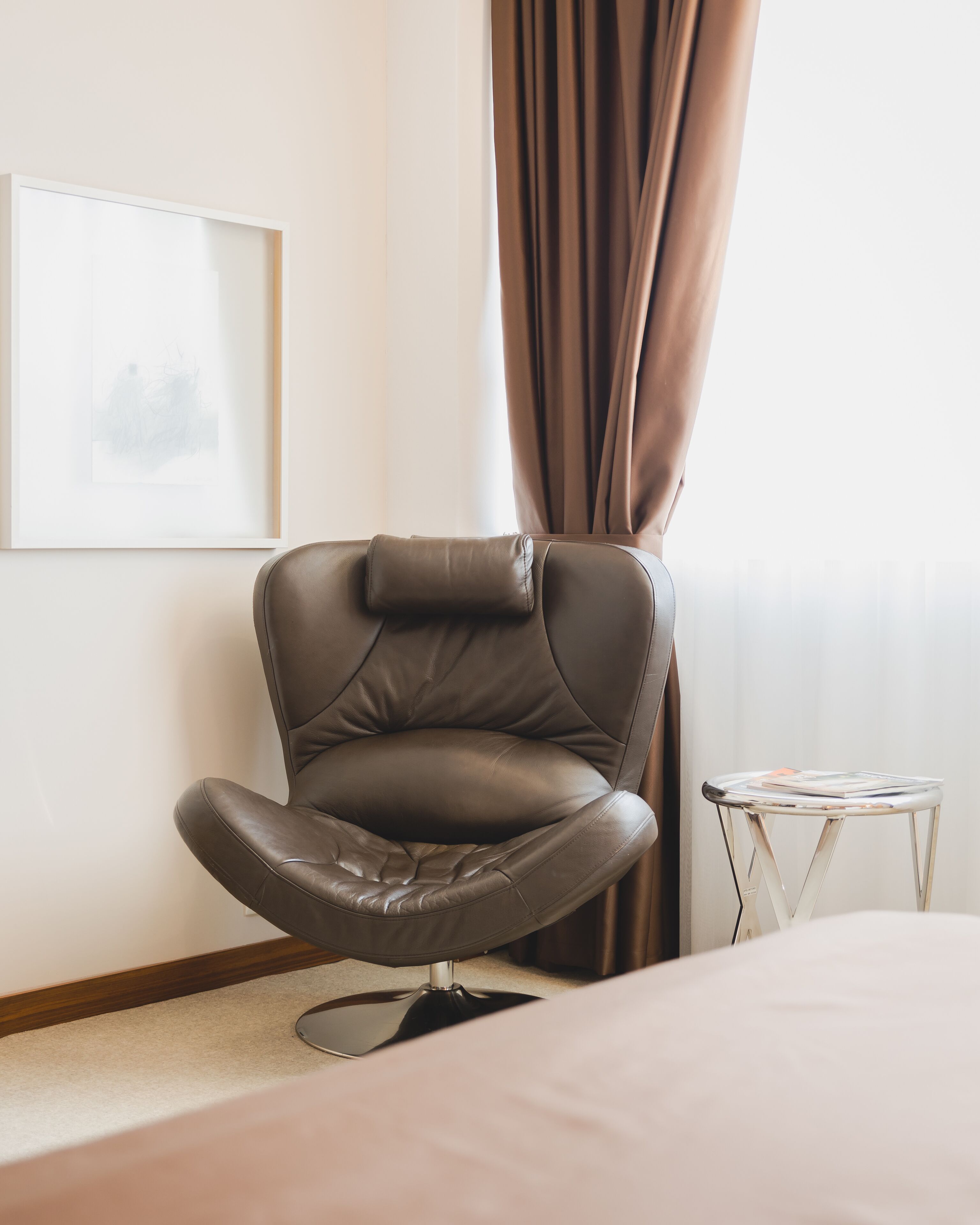 A modern room with a leather chair, a small table with a magazine, and a framed picture on the wall.