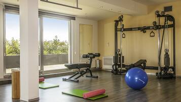 Un gimnasio amplio con diversos equipos de ejercicio, ventanas grandes y vistas al exterior.