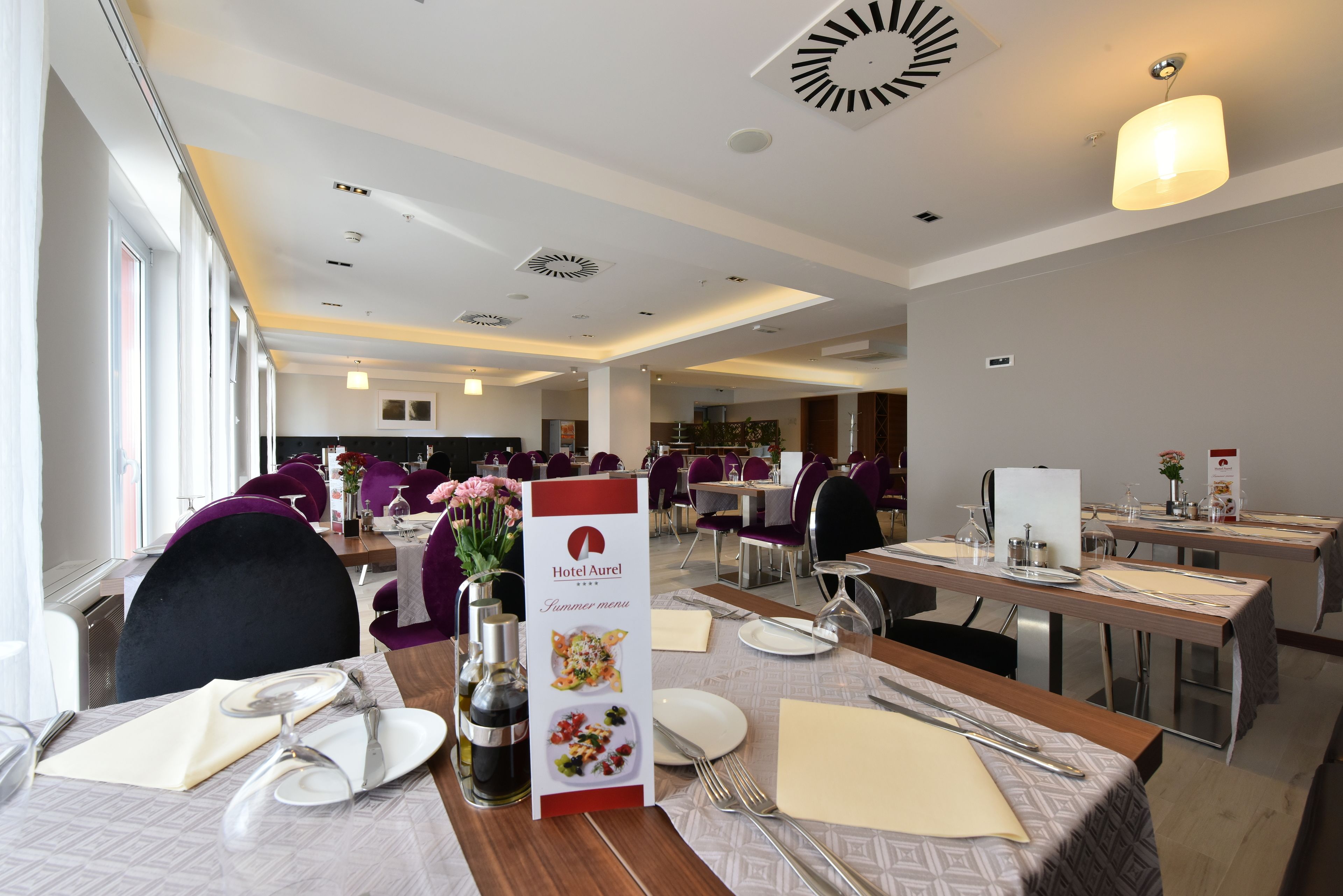 A hotel dining area with tables set for dinner, a menu stand, and purple chairs.