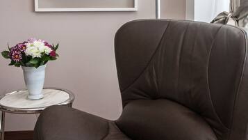 A brown leather chair, a small white vase with flowers, a framed abstract painting, and a floor lamp.