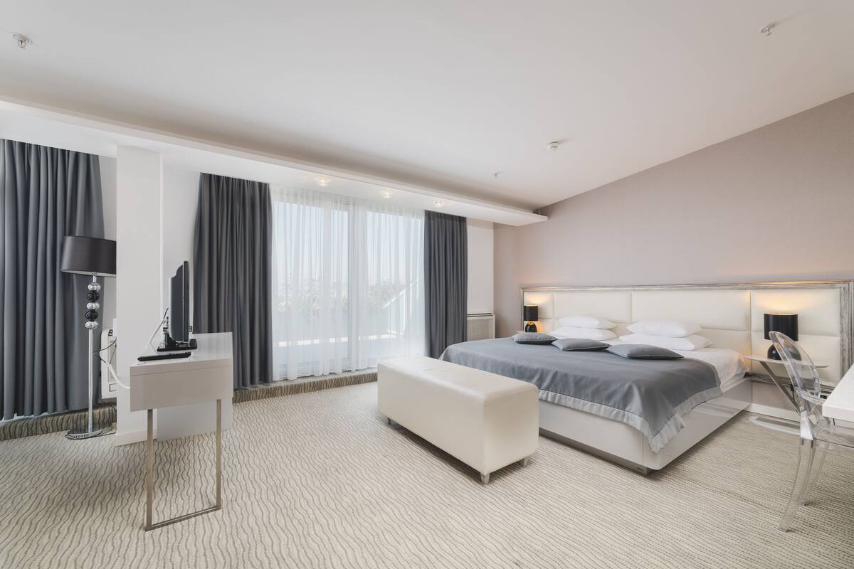 Una habitación de hotel moderna con una cama grande, un escritorio, un banco y una lámpara de pie.