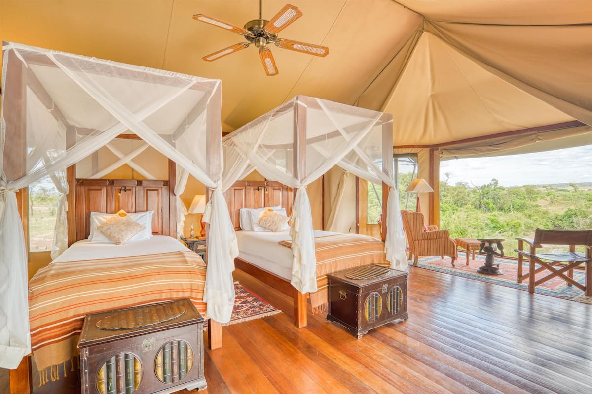 A tented accommodation with two beds, wooden furniture, and a view of the outdoors.