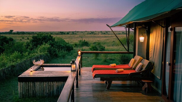 Una terraza de madera con un jacuzzi, sillas de descanso y vistas al llano al atardecer.