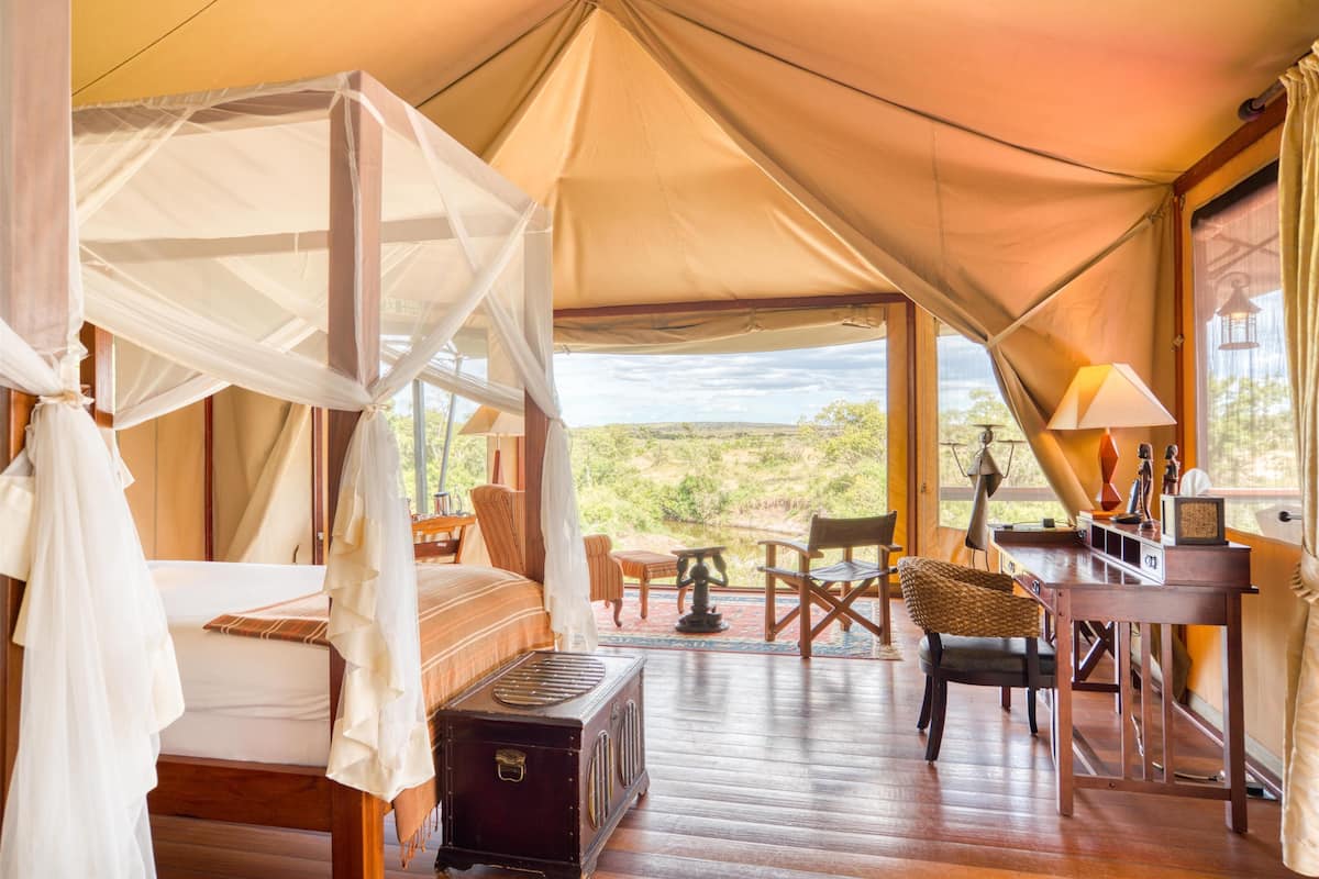 A tented room with a bed, a desk, and a view of the landscape.