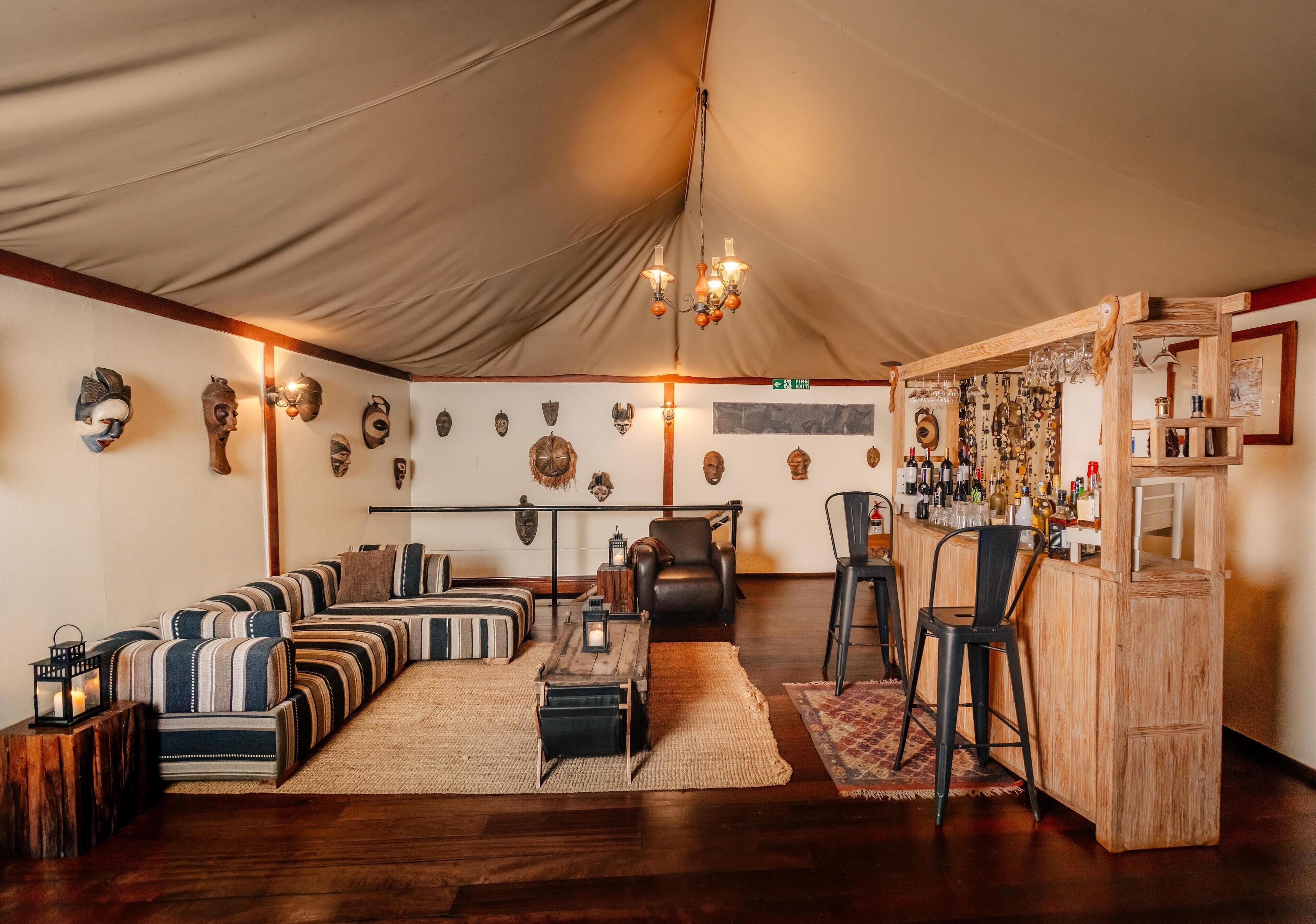 A tented room with striped sofas, a wooden bar, and various decorative masks on the walls.