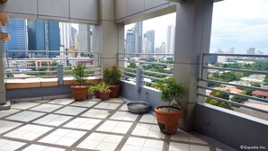 A balcony with tiled flooring, potted plants, and a view of a cityscape with tall buildings. - Lourdes Family Suites Makati powered by Cocotel (Makati)
