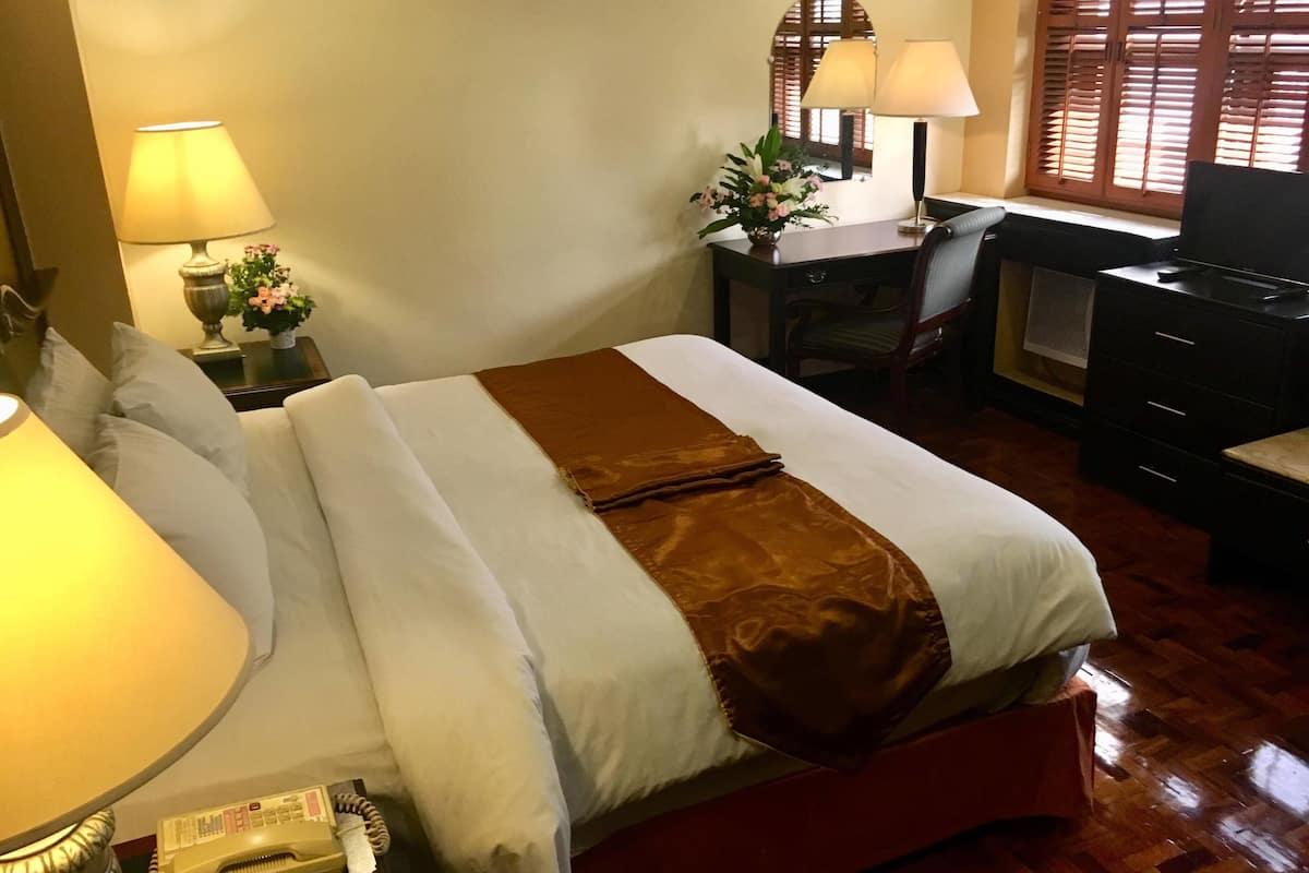 Una habitación de hotel con cama, lámparas de noche, escritorio, silla y cómoda.