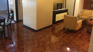 A hotel room with a wooden parquet floor, a dining area with a table and chairs, a sofa, and a TV on a cabinet. - Lourdes Family Suites Makati powered by Cocotel (Makati)