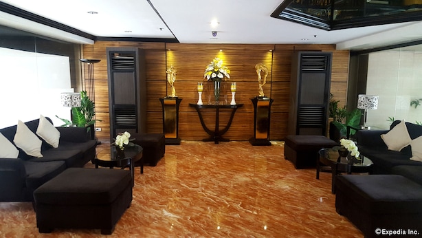 A lobby with a marble floor, black sofas, a central table with a vase, and wooden panel walls. - Lourdes Family Suites Makati powered by Cocotel (Makati)