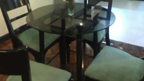 A dining area with a glass table surrounded by chairs, a vase with flowers, and a kitchen in the background. - Lourdes Family Suites Makati powered by Cocotel (Makati)