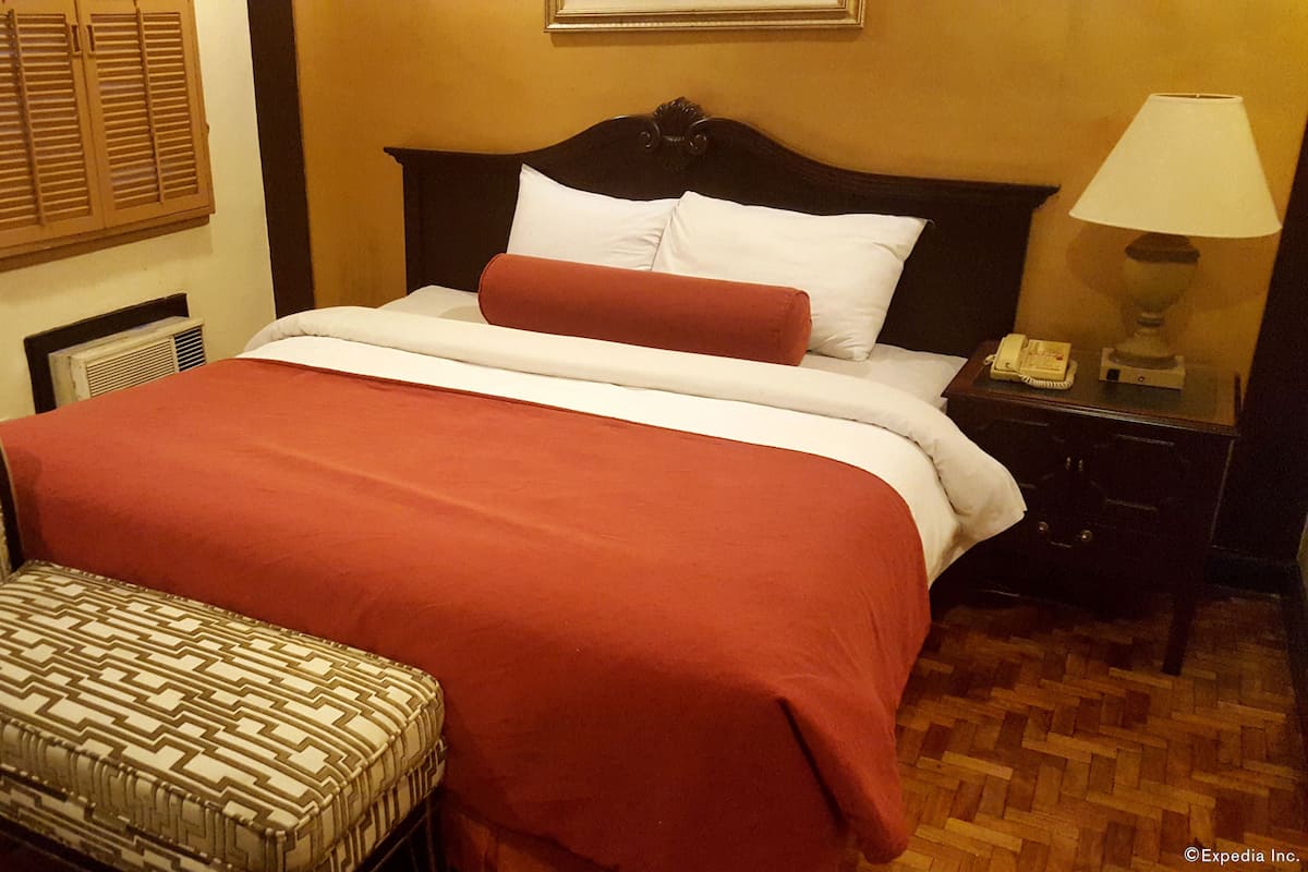 Una habitación de hotel con una cama, una silla, una mesita de noche y una lámpara.