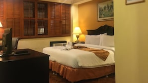 A hotel room with a bed, a desk with a computer, a lamp, and a painting on the wall. - Lourdes Family Suites Makati powered by Cocotel (Makati)