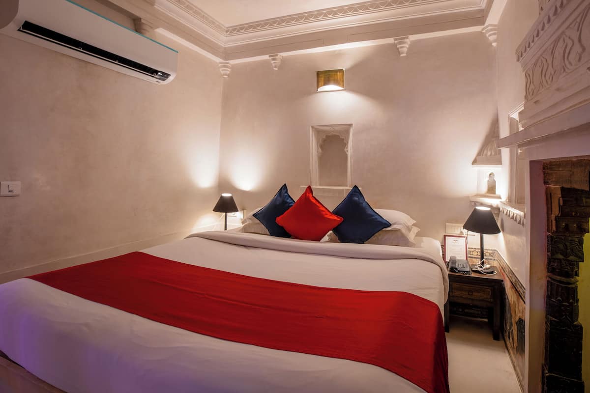 Habitació d'hotel amb un llit gran, dues làmpades de nit, una tauleta de nit i aire condicionat fixat a la paret.