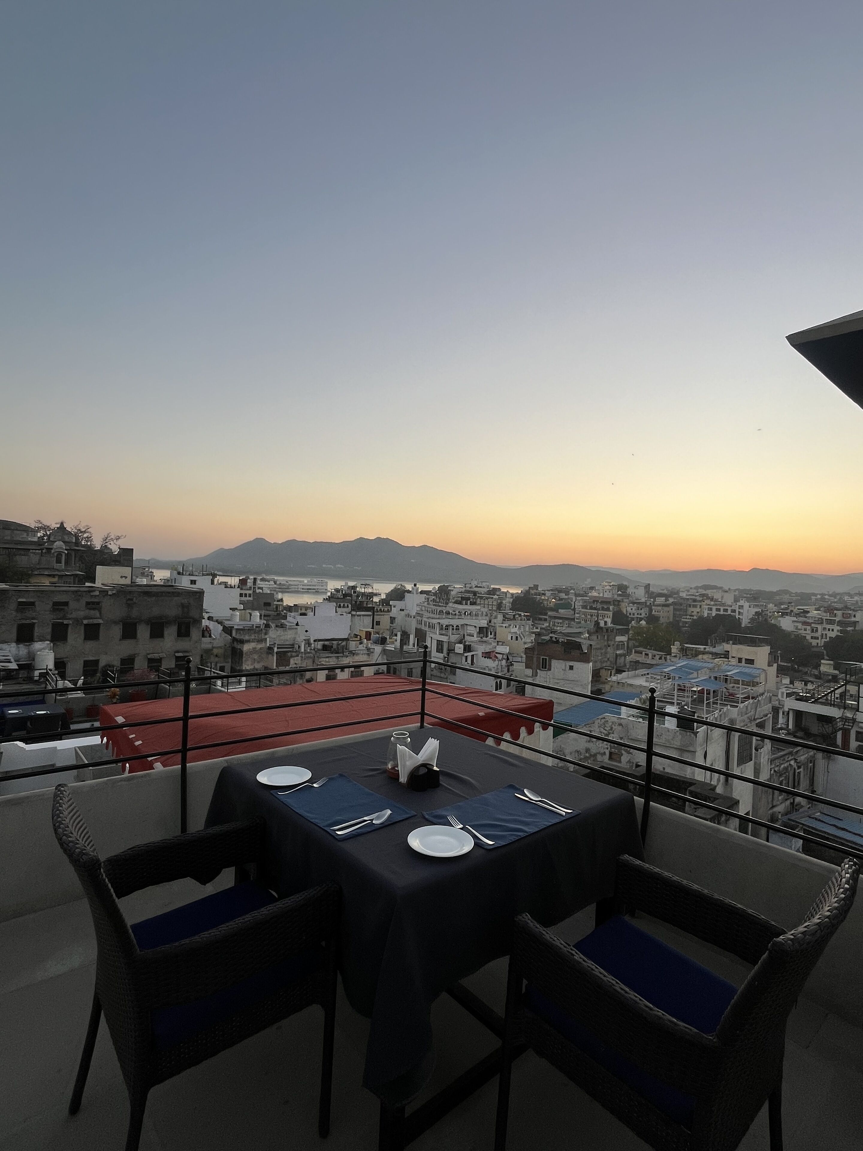 A table set for two on a balcony with a cityscape view in the background.