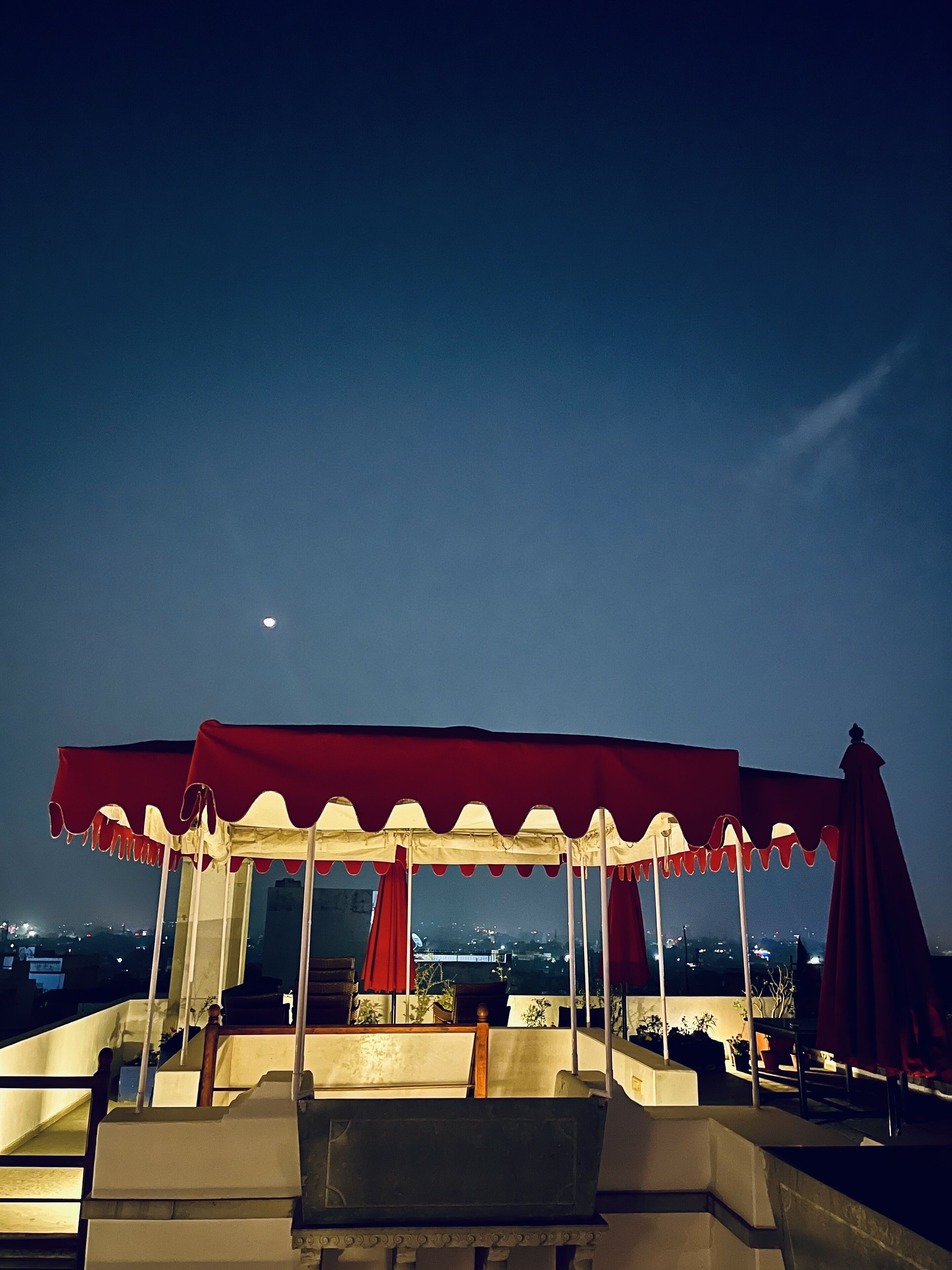 Una terraza en la azotea con toldo rojo, zona de estar y vistas a la ciudad de noche.