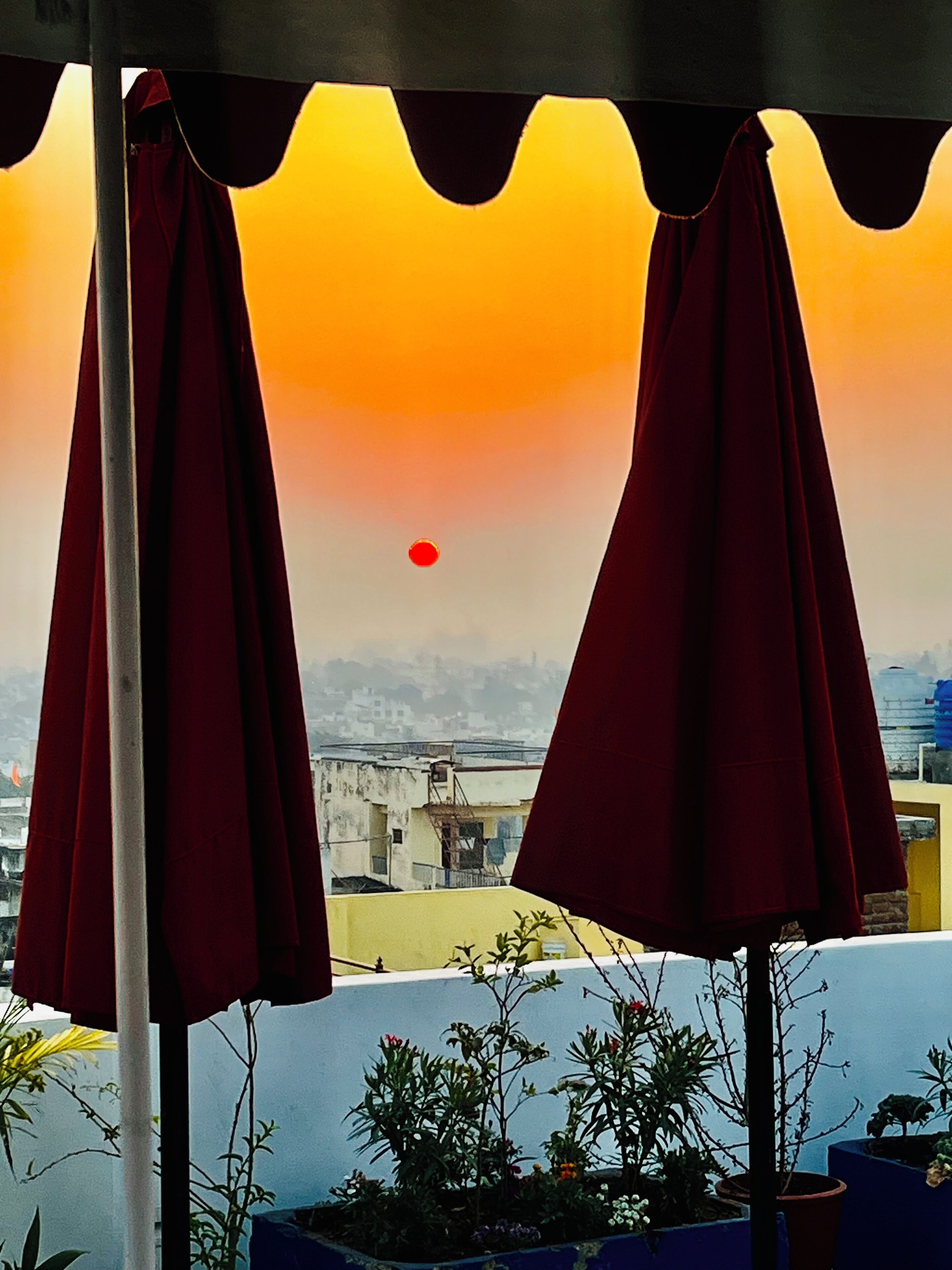 A balcony with red umbrellas, a view of buildings, and a sunset.