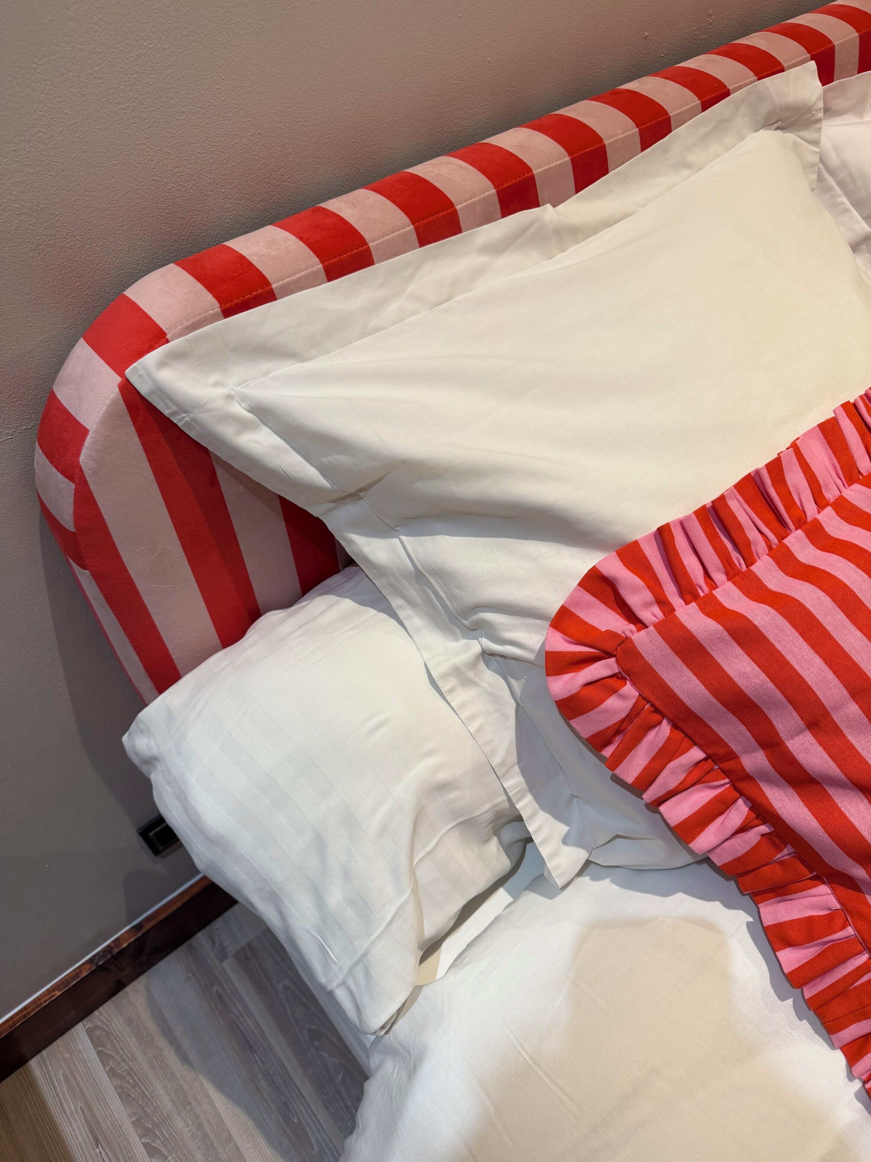Una cama con almohadas a rayas y una colcha blanca.