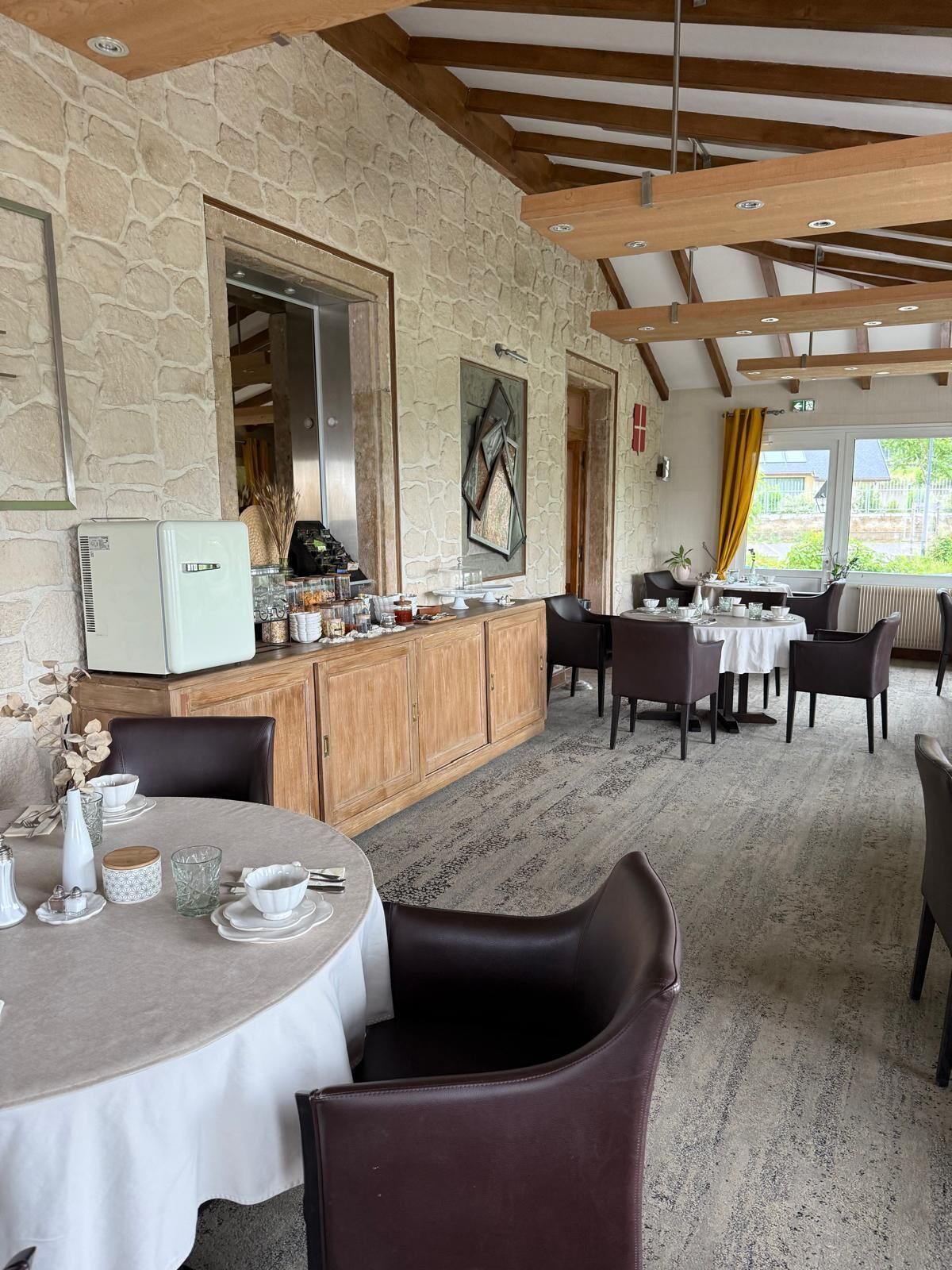 Un ristorante con pareti in pietra, travi in legno e un assortimento di tavoli rotondi e rettangolari.