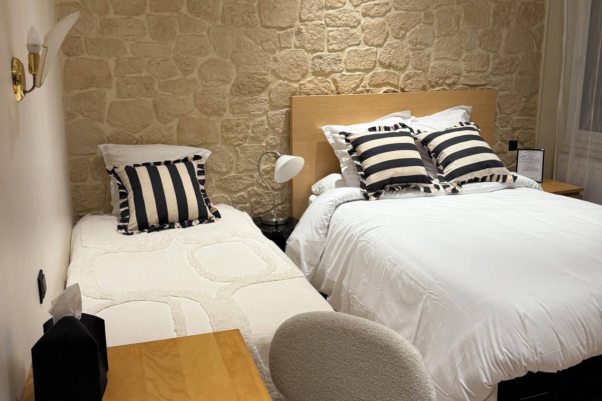 Une chambre avec deux lits, un bureau en bois et un mur en pierre.