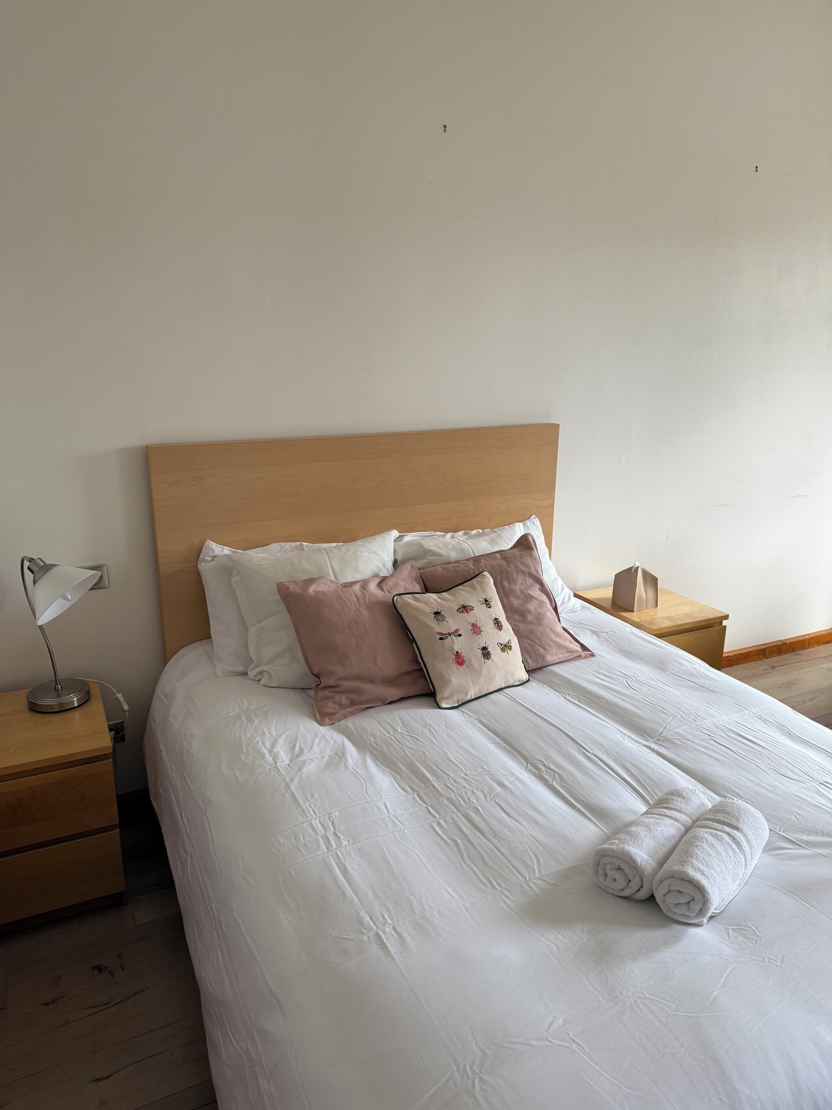 A neatly made bed with white bedding and two pillows, one with a floral design.